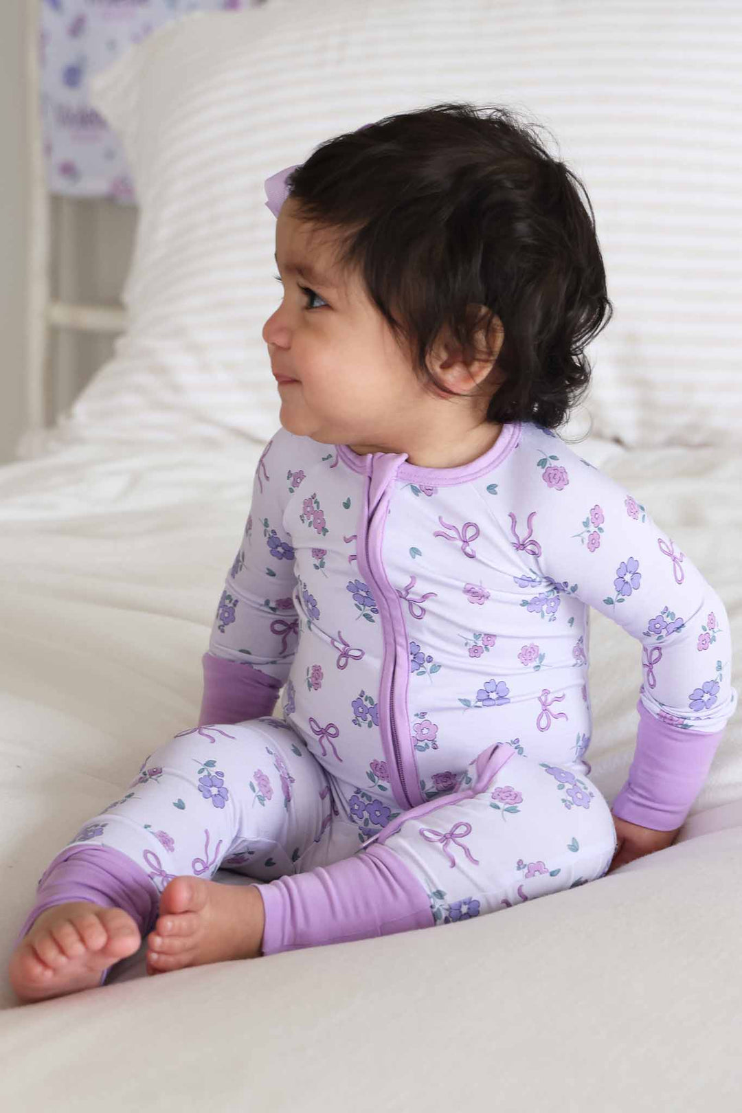 girl sitting on bed in purple ribbon and roses convertible zip romper 