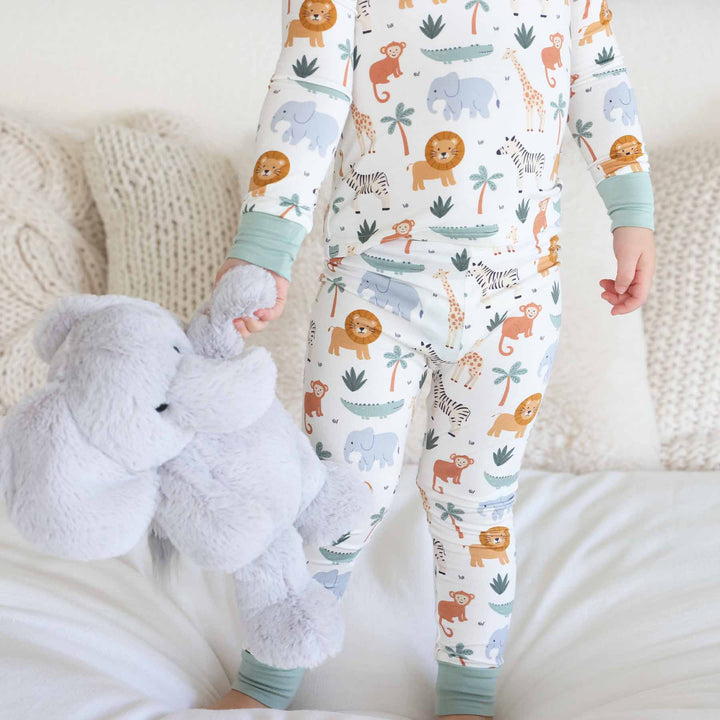 kid wearing safari animal two piece pajama set holding an elephant stuffed animal 