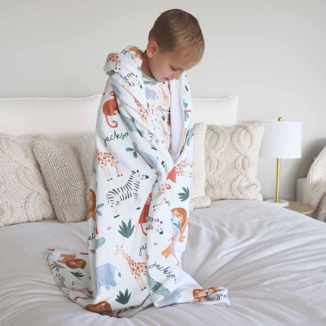 boy standing on bed wrapped in a personalized safari themed blanket 
