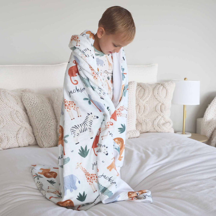 boy standing on bed wrapped in a personalized safari themed blanket 