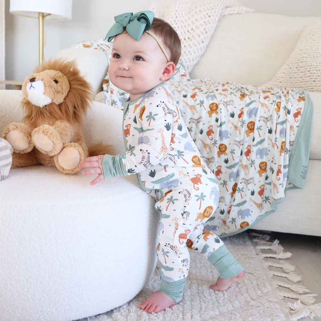 standing toddler girl wearing safari animal pajama romper with lion stuffed animal