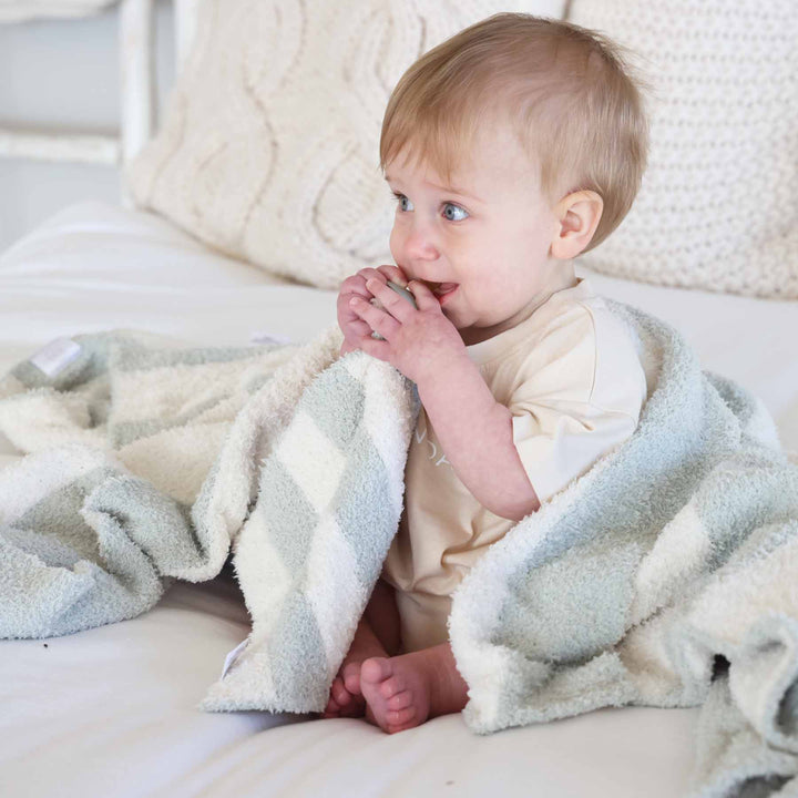 baby boy sitting on a bed holding a green and white striped plush lovey with a matching  blanket draped over him 