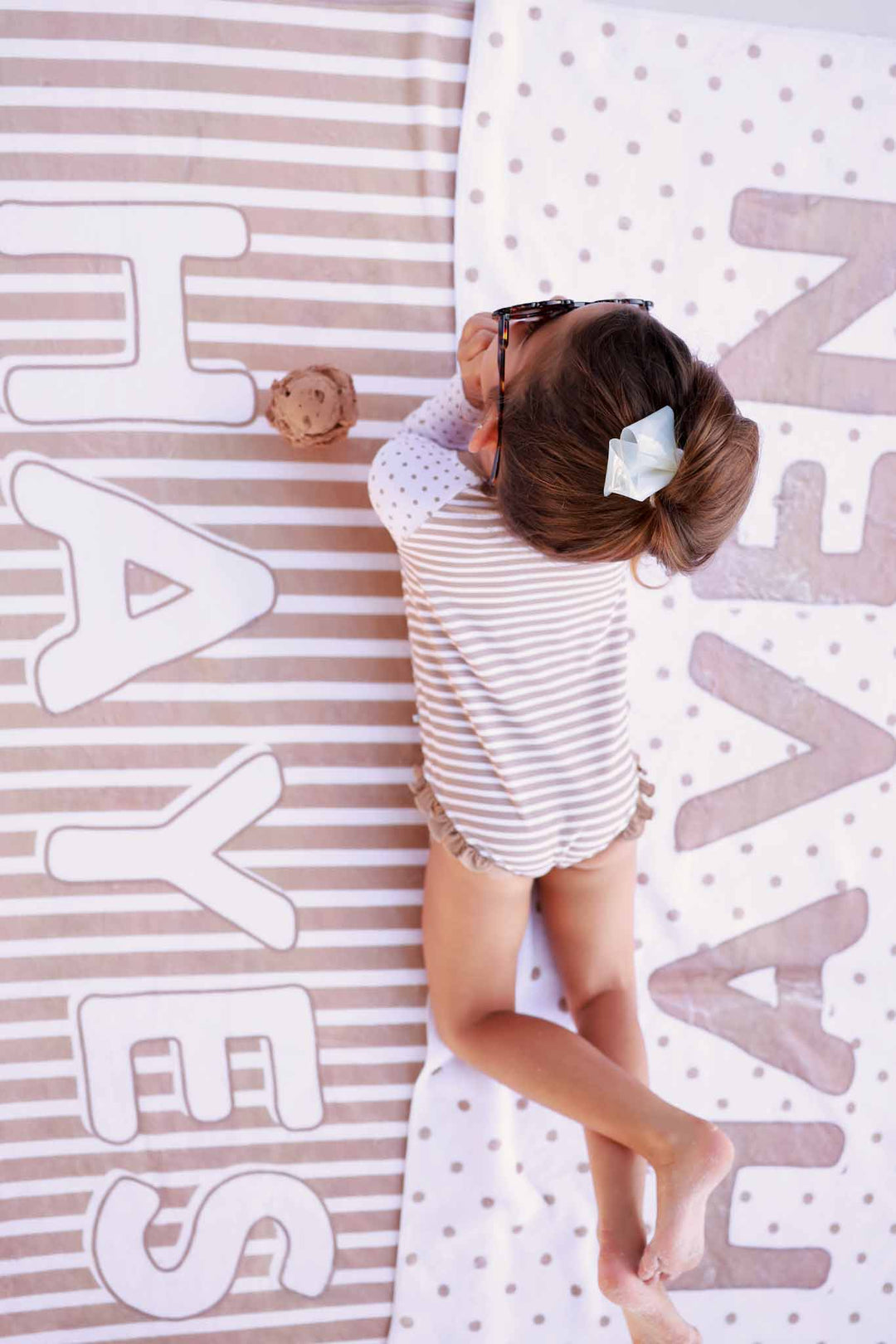 girl laying on two beach towels that have stripes and polka dots 