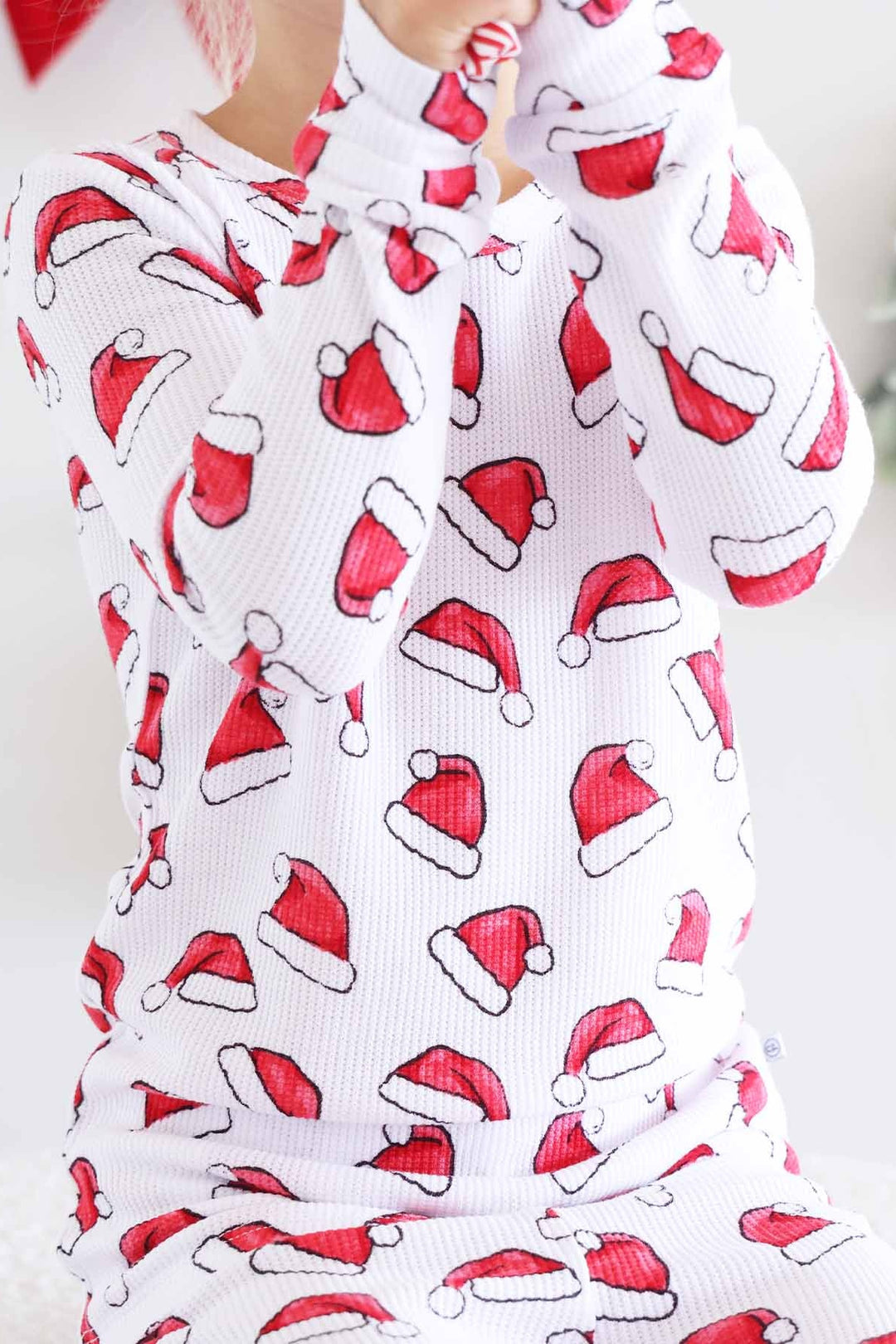 Child in a Caden Lane two-piece Christmas pajama set with a festive Santa hat