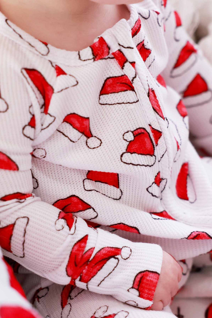 Toddler wearing a Caden Lane white waffle-knit zip romper with a festive red Santa hat print 