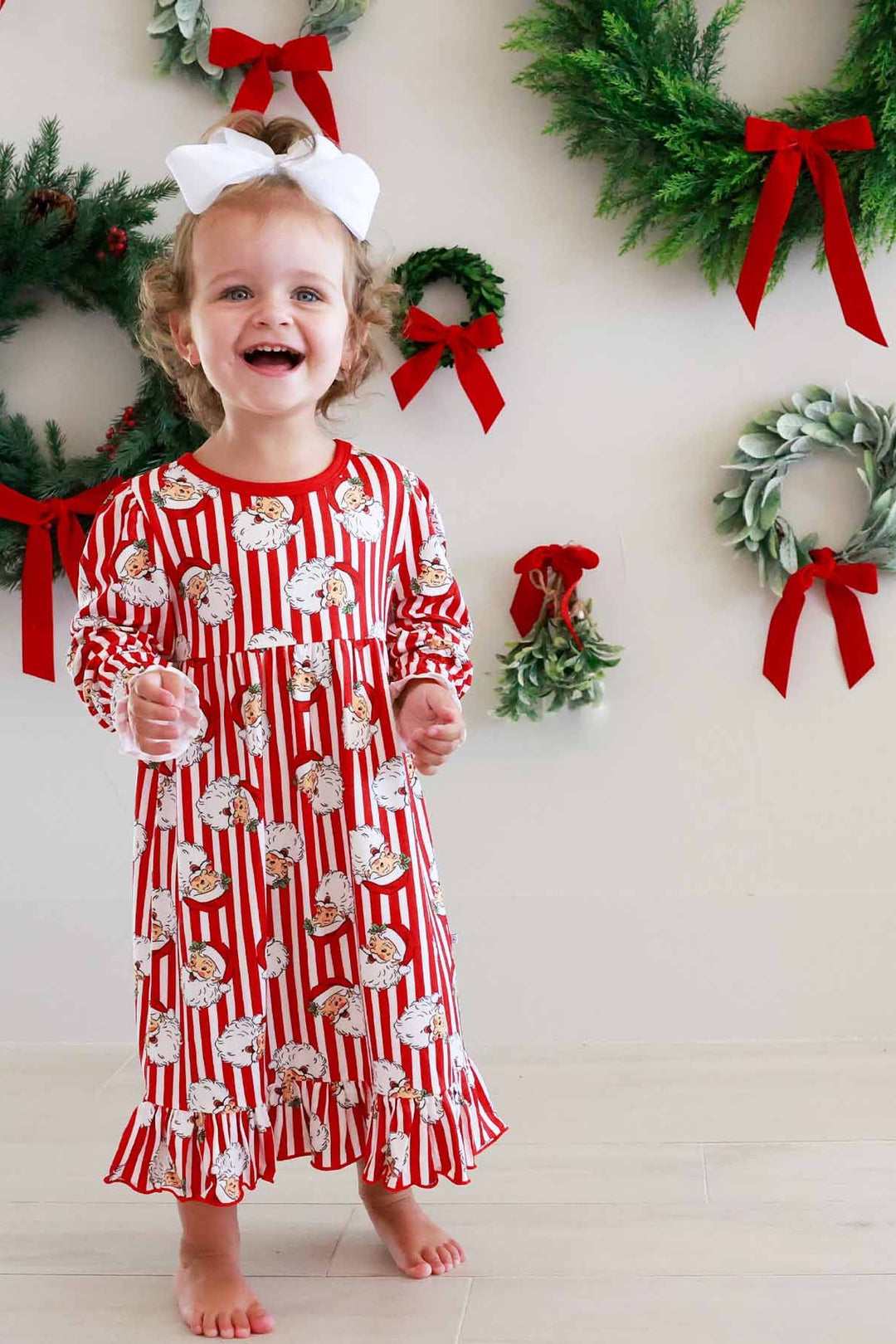 Girl in Caden Lane Christmas nightgown featuring a classic red and white vertical stripe print with vintage Santa faces, long sleeves with ruffle cuffs, a gathered empire waist, and a ruffle hem