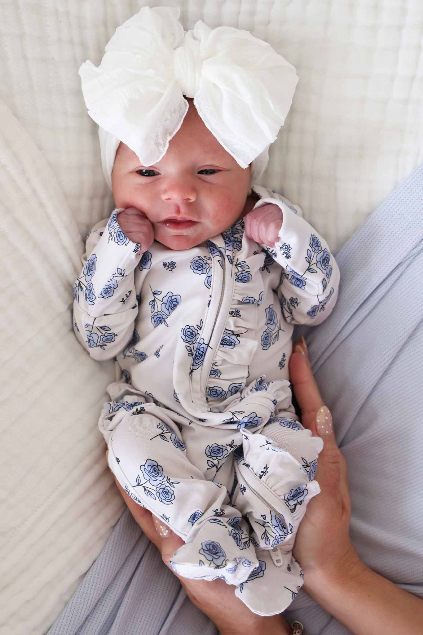 newborn baby girl in blue rose ruffle zipper footie with white large ruffle knit bow 