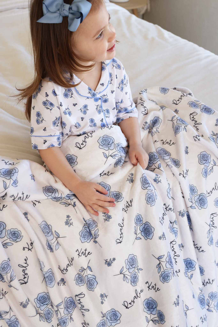 girl sitting on bed with blue rose personalized blanket on her lap 