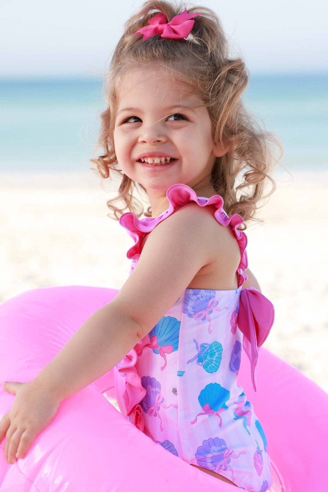 girl standing in inner tube with colorful seashell ruffled one piece swimsuit