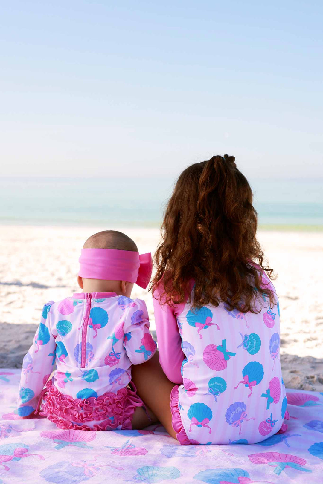 two girls sitting on the beach in matching seaside sweetie swimsuits 