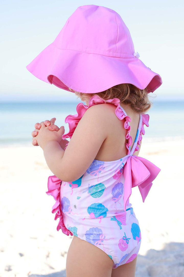 girl standing on beach in seaside sweetie double ruffle swimsuit with matching solid pink sun hat 