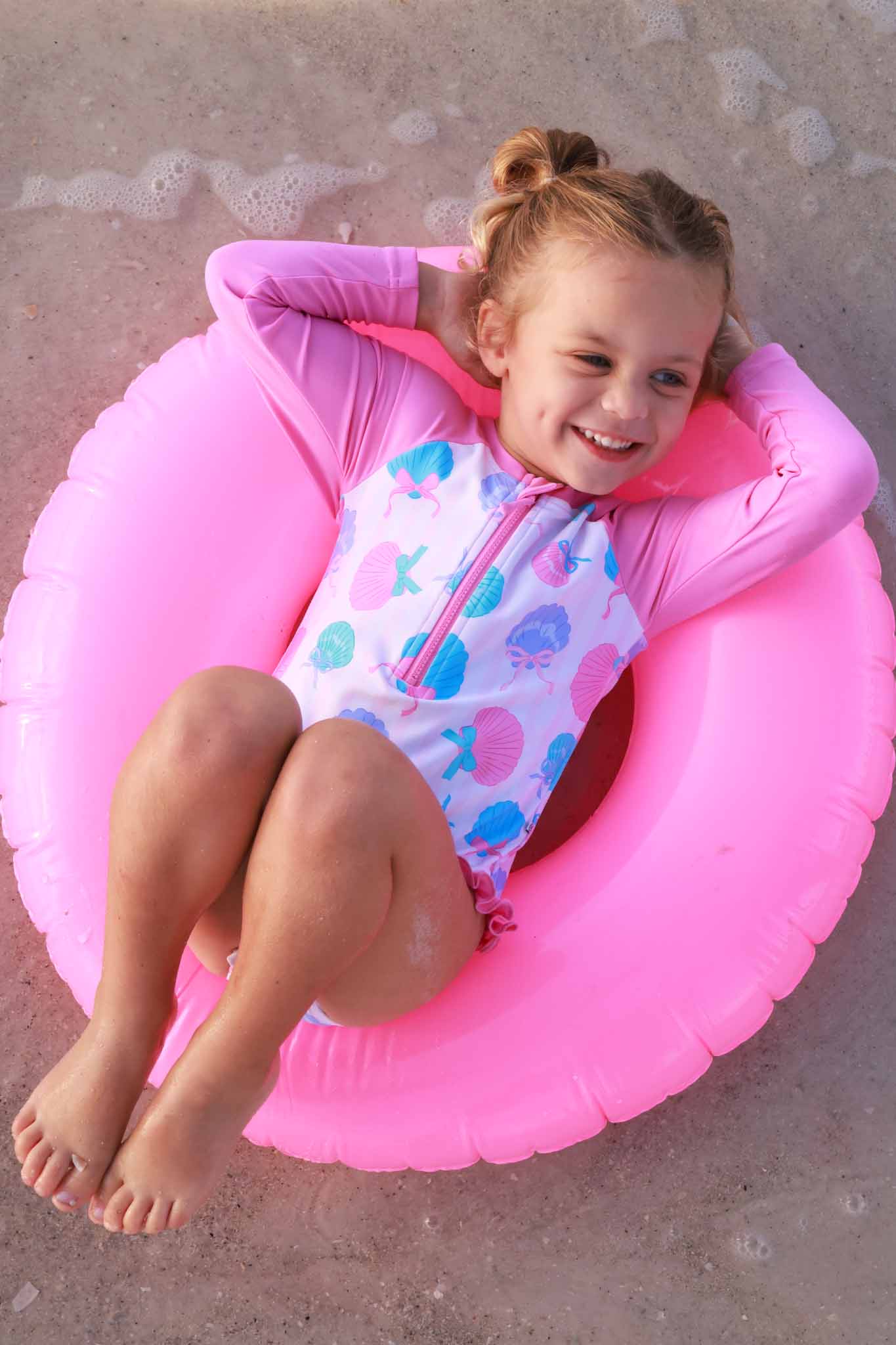 girl laying in inner tube in seaside sweetie long sleeve rash guard swimsuit 