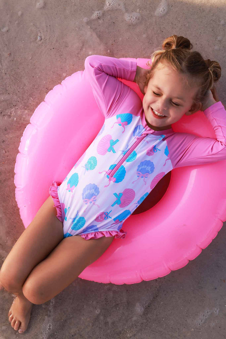 girl laying on inner tube in girly seashell long sleeve romper swimsuit 