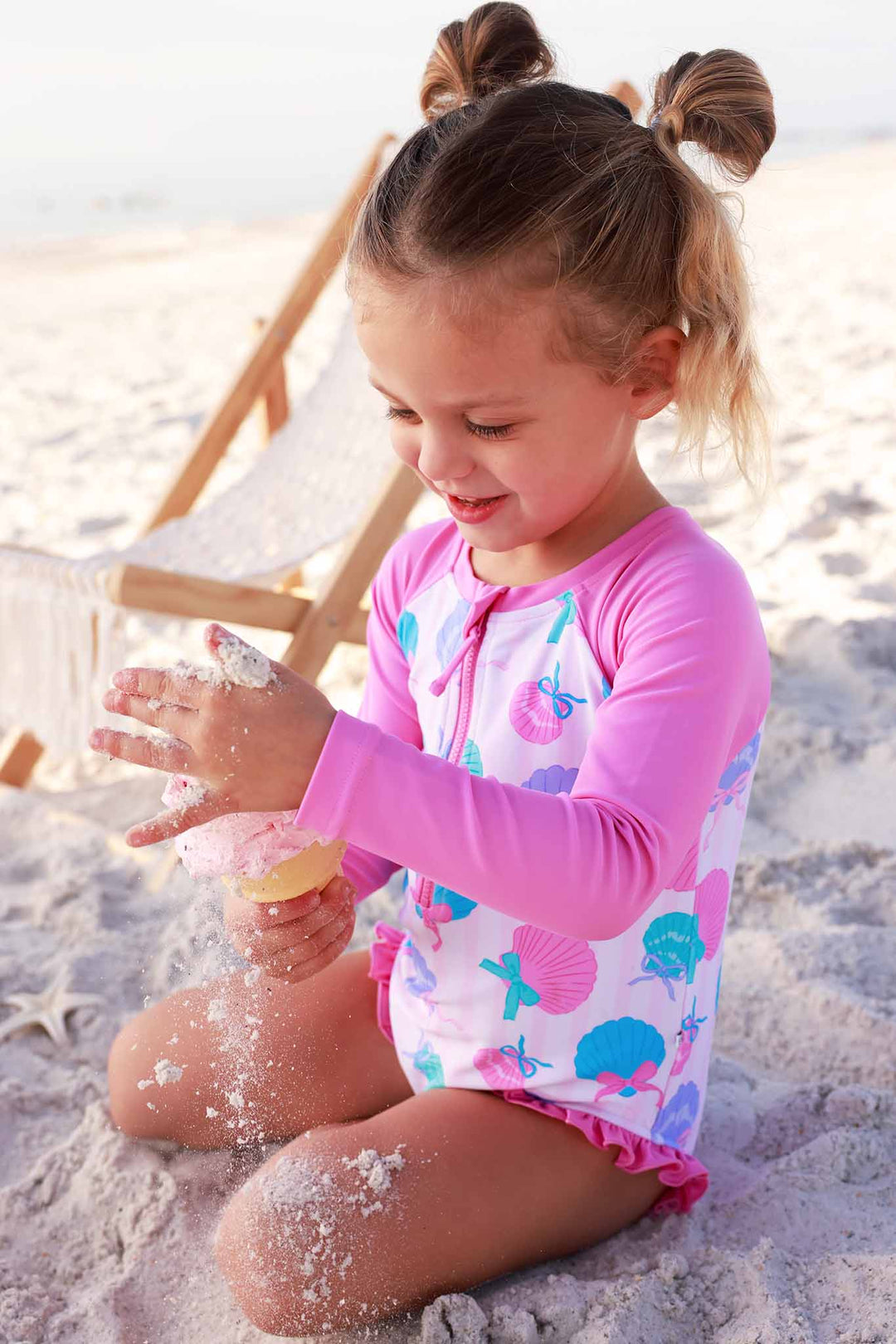girl playing with sand and eating ice cream in seaside sweetie rash guard swimsuit 