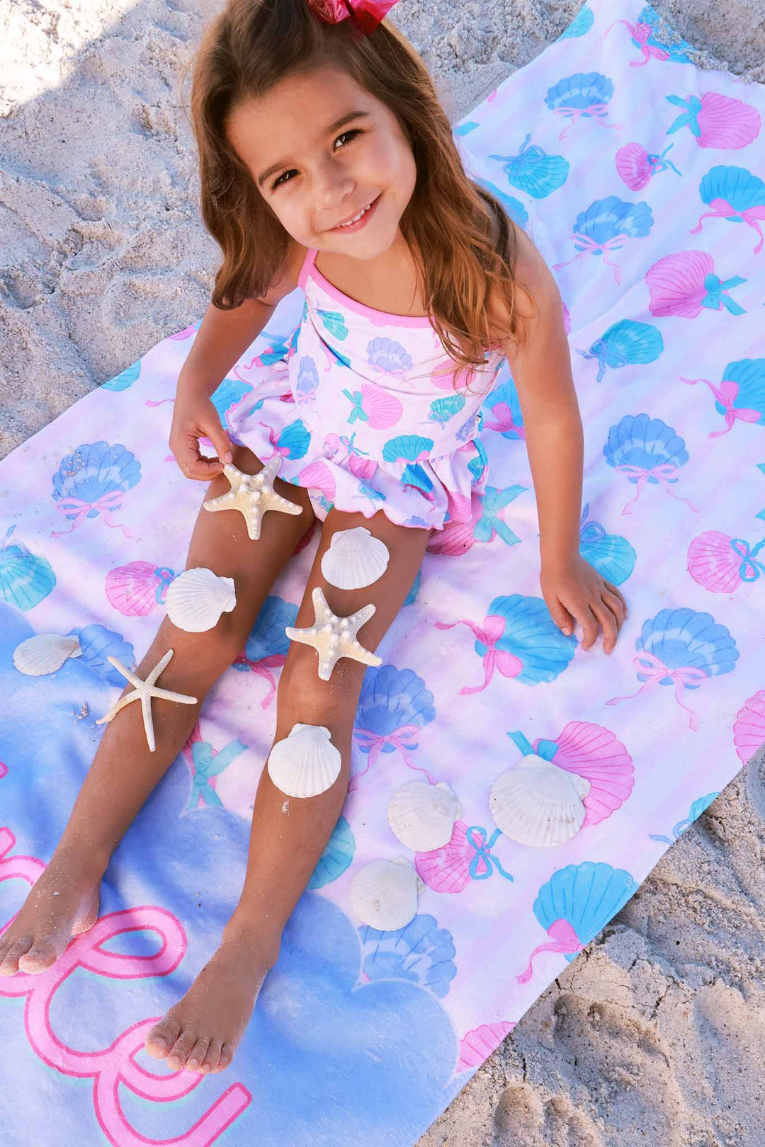 girl sitting on personalized beach towel with seashells on her legs