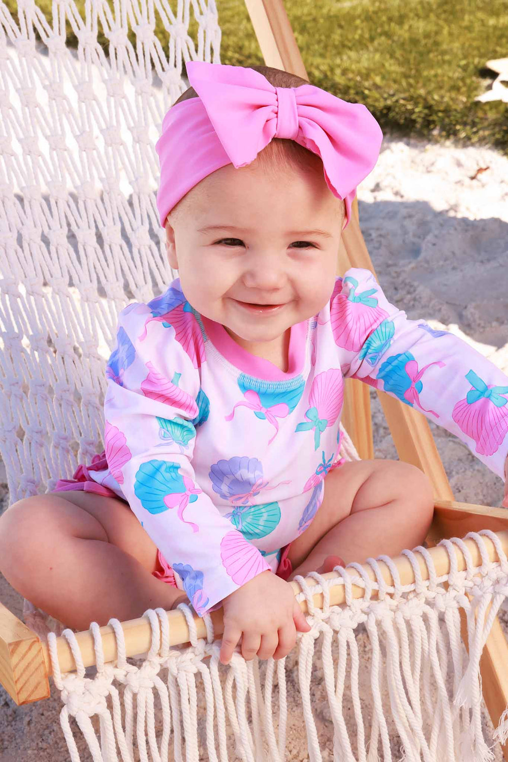 girl sitting on beach chair in seashell long sleeve rash guard with ruffle bottom with matching pink swim bow