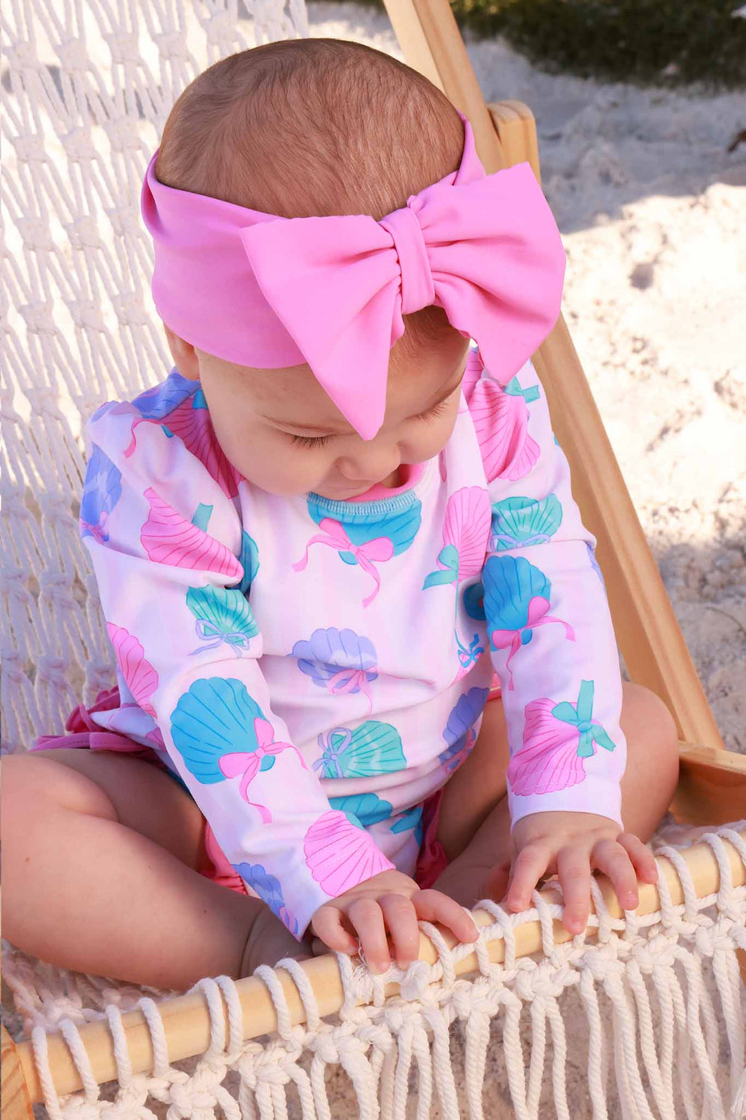 baby girl wearing the seaside sweetie rash guard swimsuit for girls with pink ruffles on the bottom and matching headwrap