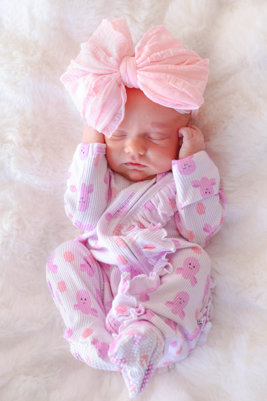 newborn in sea snuggles bamboo waffle ruffle zipper footie on white fur with pink bow headband — front lifestyle view