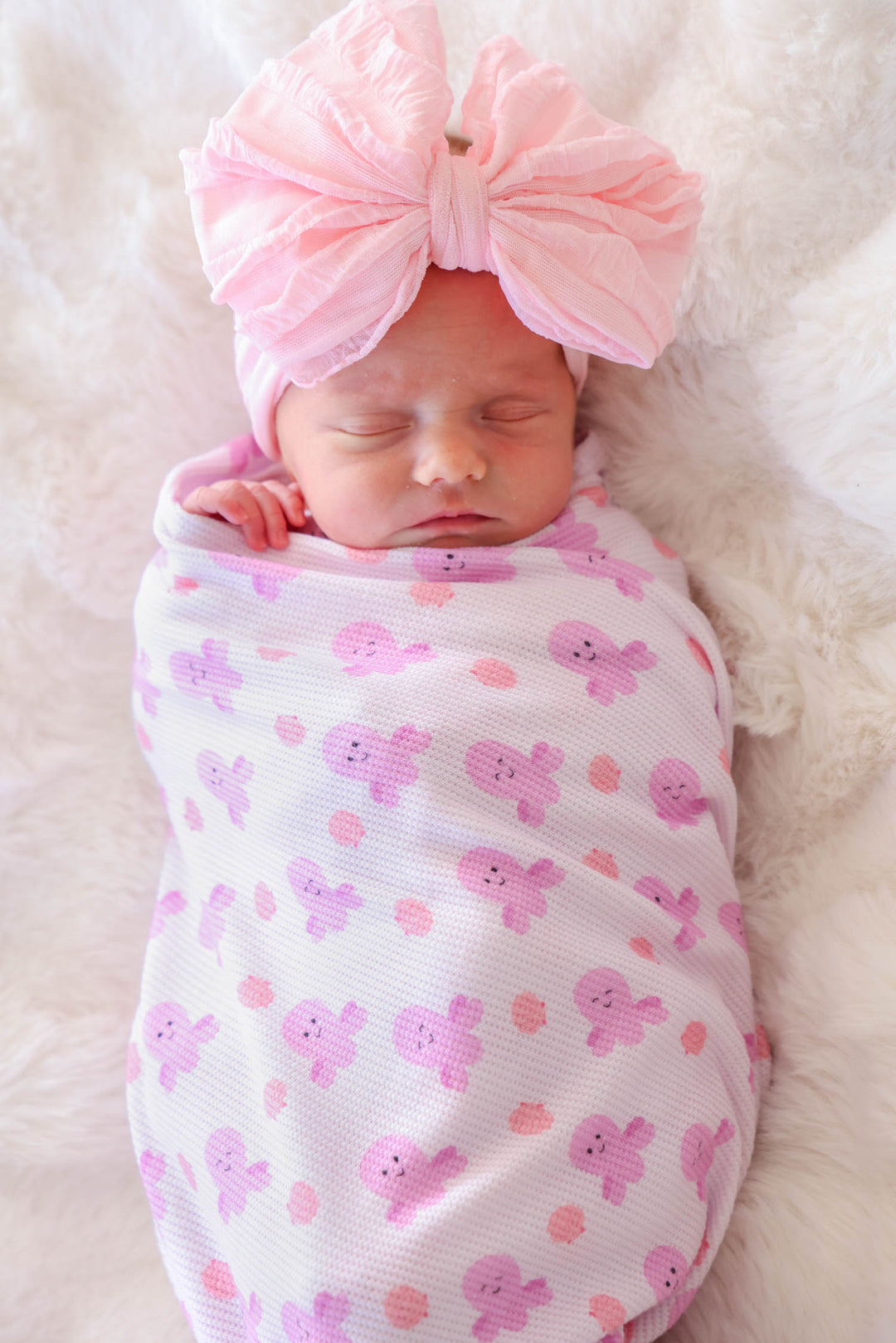 newborn swaddled in sea snuggles bamboo waffle oversized swaddle blanket on white fur with large pink bow headband