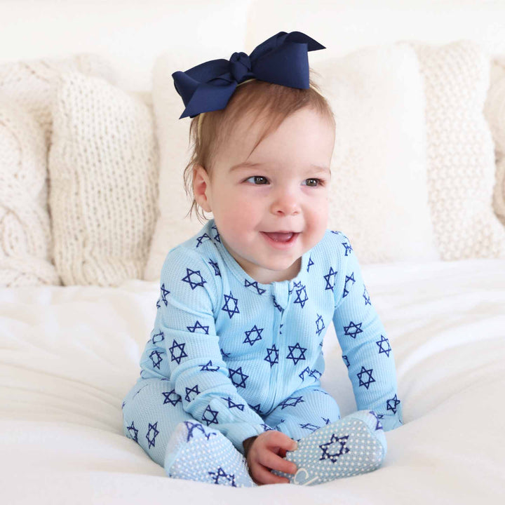 baby girl wearing blue star of david pajamas with bamboo waffle fabric and a navy ribbon bow headband 