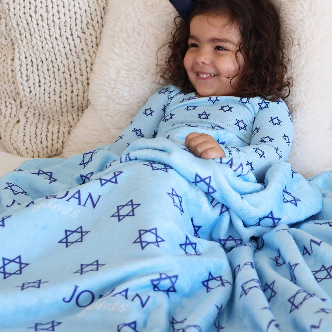 girl wearing star of david pajamas and is covered in a star of david personalized blanket 