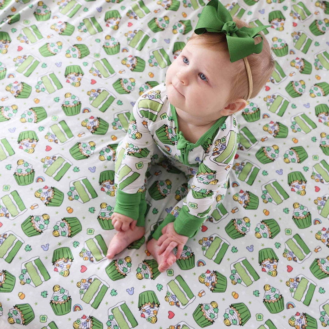 Baby wearing the St. patrick's day green ribbon bow headband for girls and sitting on the shamrock sweets blanket