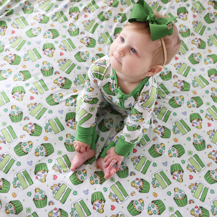 Baby wearing the St. patrick's day green ribbon bow headband for girls and sitting on the shamrock sweets blanket