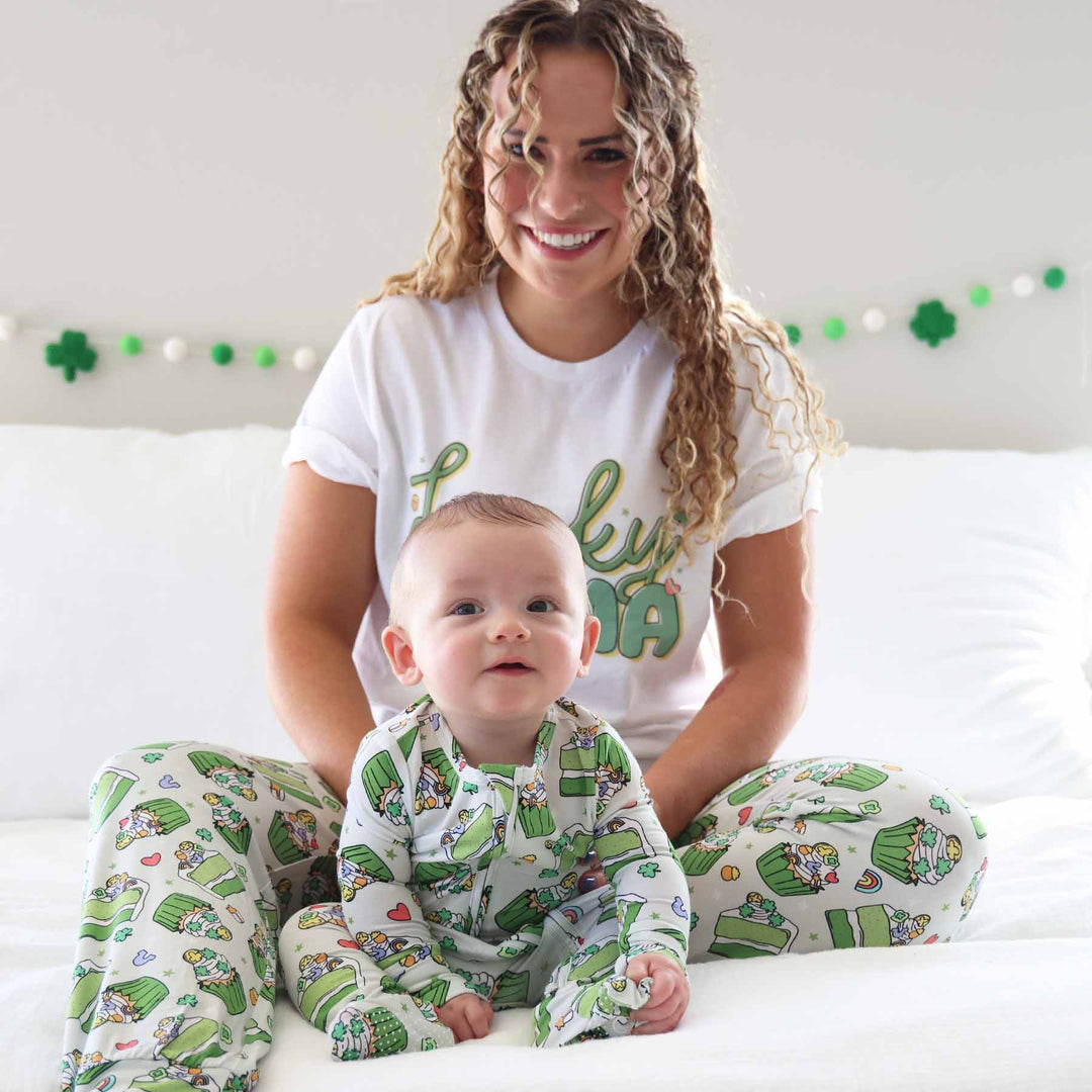 baby boy sitting on bed in front of mom in shamrock sweet st. patrick's day pajamas with matching adult pajama pants 