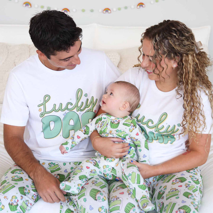 mom and dad wearing matching t-shirt and pajama pants for st. patrick's day with a baby sitting on their lap wearing a matching footie