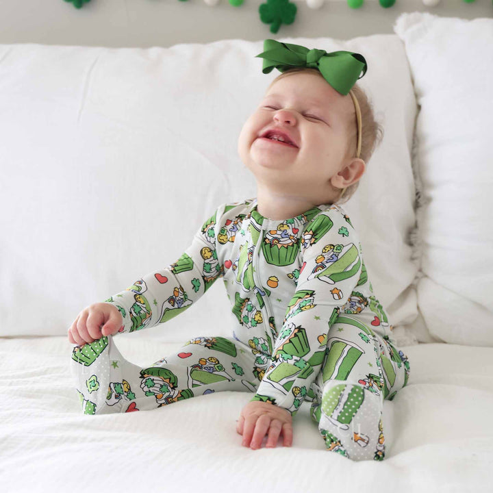 baby girl wearing a st patick's day dessert zipper footie pajama with a matching green ribbon bow headband 
