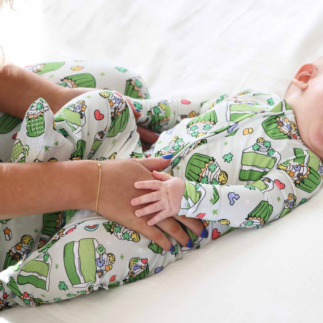 baby laying down wearing a st. patrick's day sweets green footie pajama with mom wearing matching pajama pants 