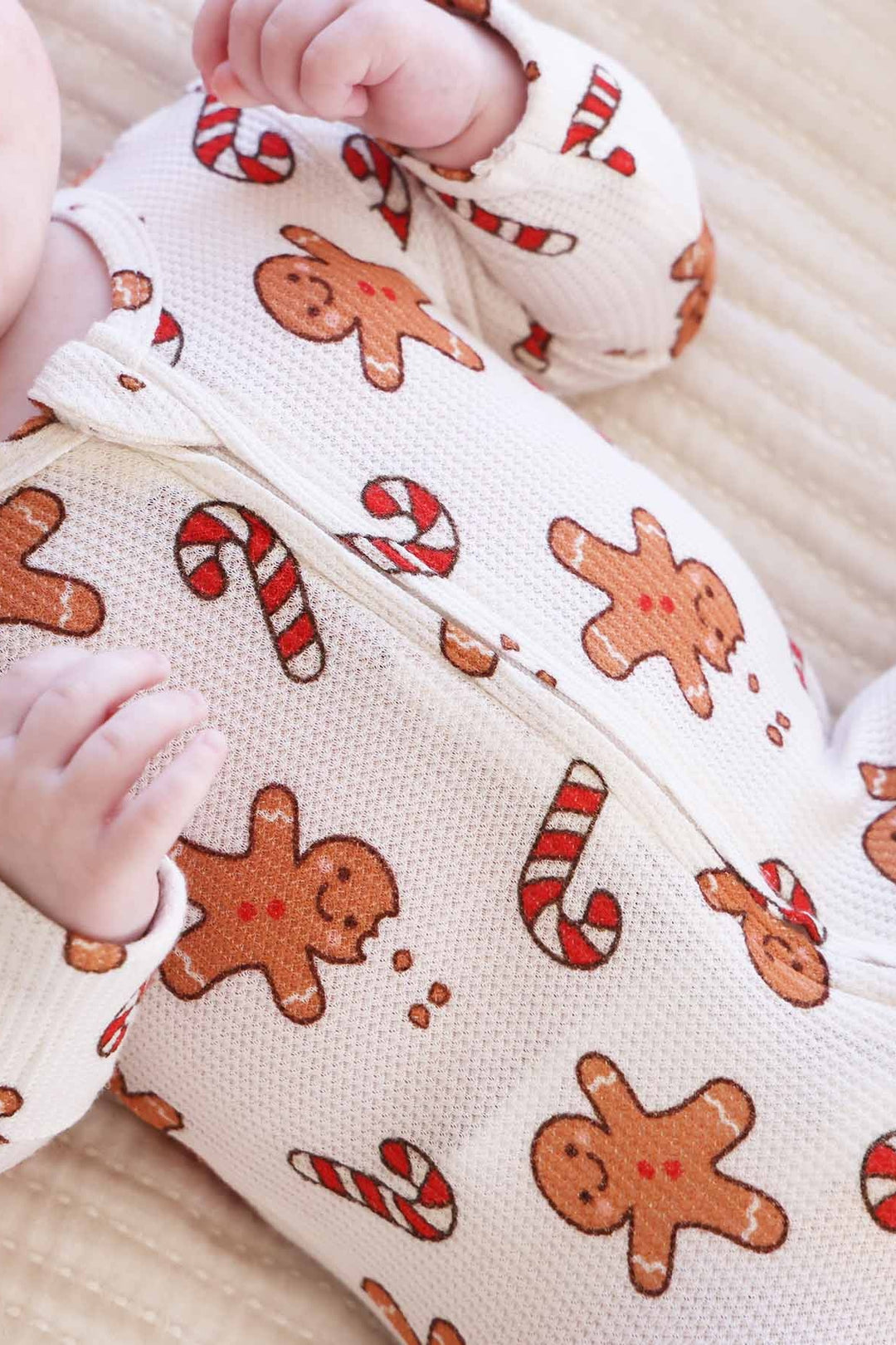 Smiling baby wearing a Caden Lane gingerbread and candy cane holiday footie pajamas on a cozy white blanket