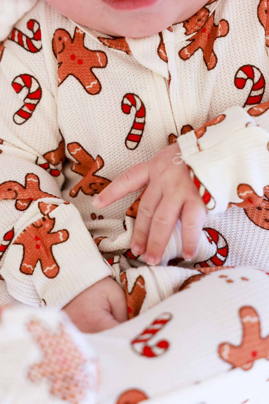 Smiling baby wearing a Caden Lane gingerbread and candy cane holiday footie pajamas