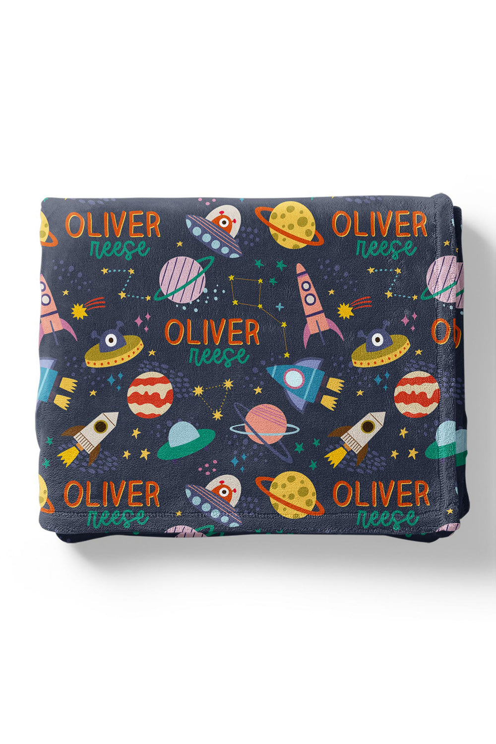 Flat lay of a folded personalized Caden Lane Star Explorer blanket in navy, showing planets, rockets, UFOs, and custom name print
