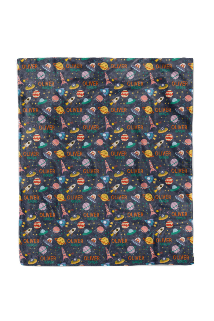 Flat lay of a fully unfolded personalized Caden Lane Star Explorer blanket in navy, showing the full repeating pattern of planets, rockets, and custom name