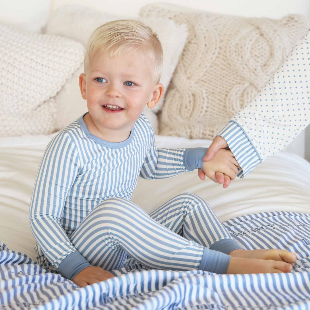 boy wearing a blue and white stripe long sleeve pajama set with mom holding his hand in coordinating polka dot lounge set with stripe detailing on sleeves