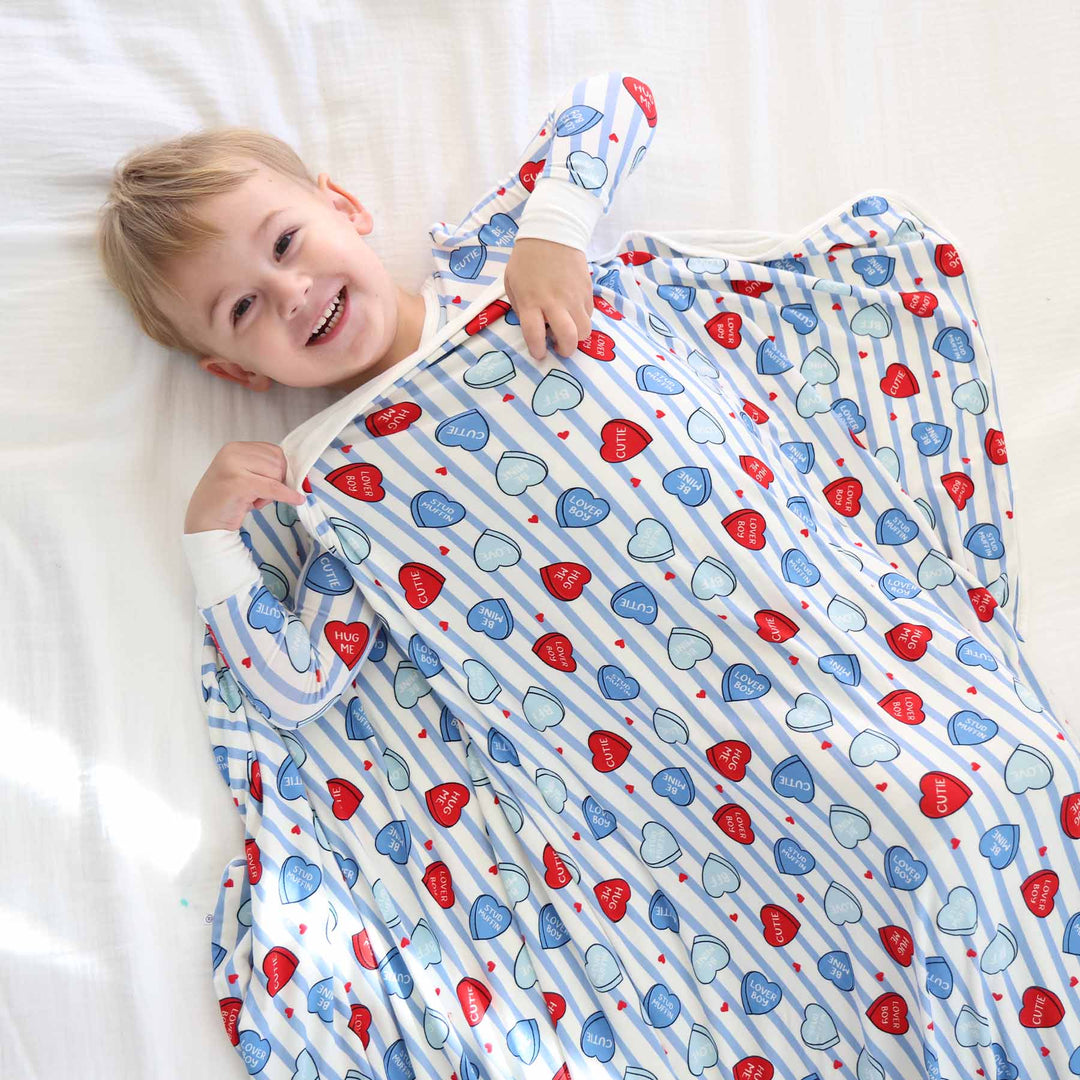 boy laying on a bed with a conversation heart and blue stripe double sided bamboo blanket for kids