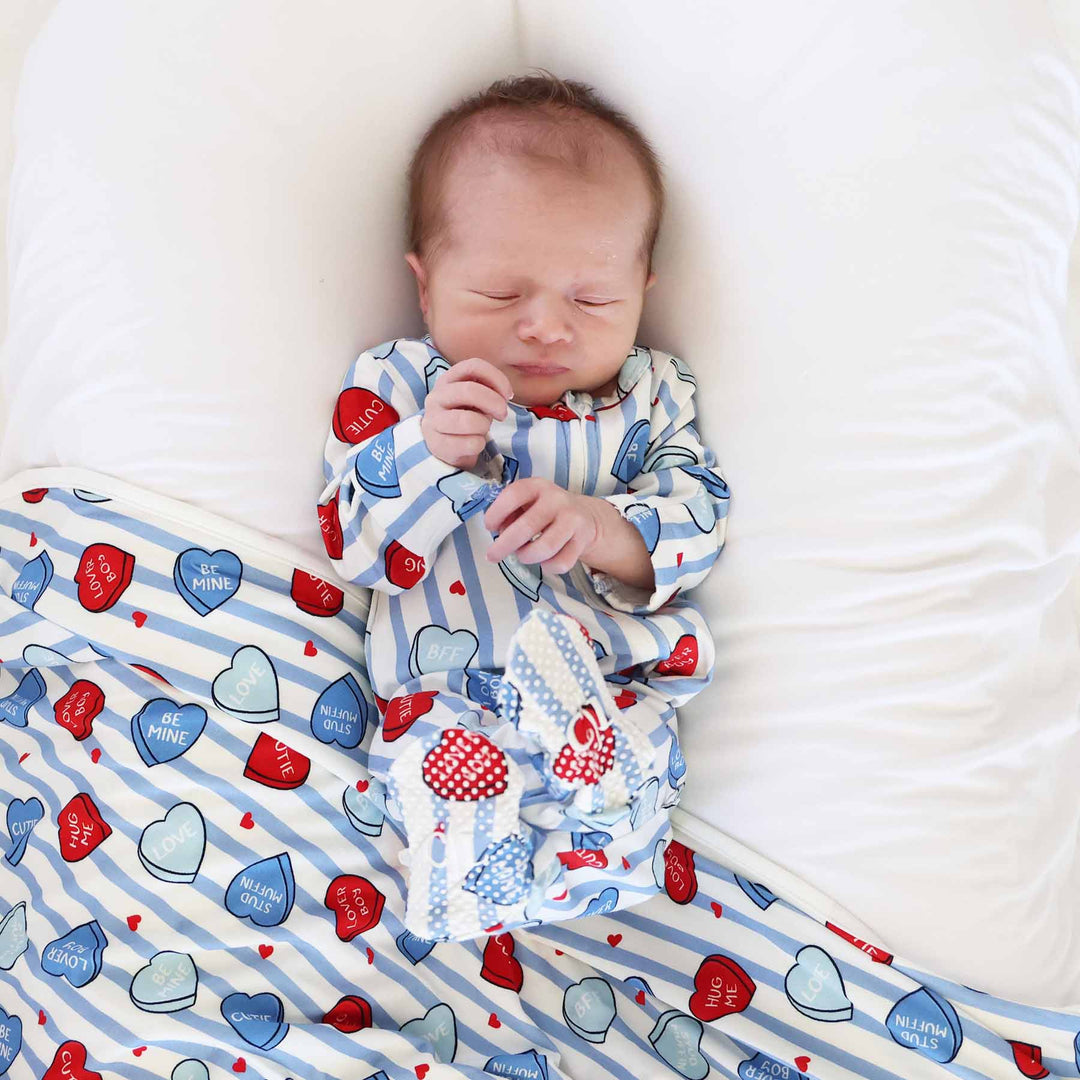 baby laying on a bed wearing a blue stripe heart candy footie for valentine's day with a matching bamboo blanket underneath him