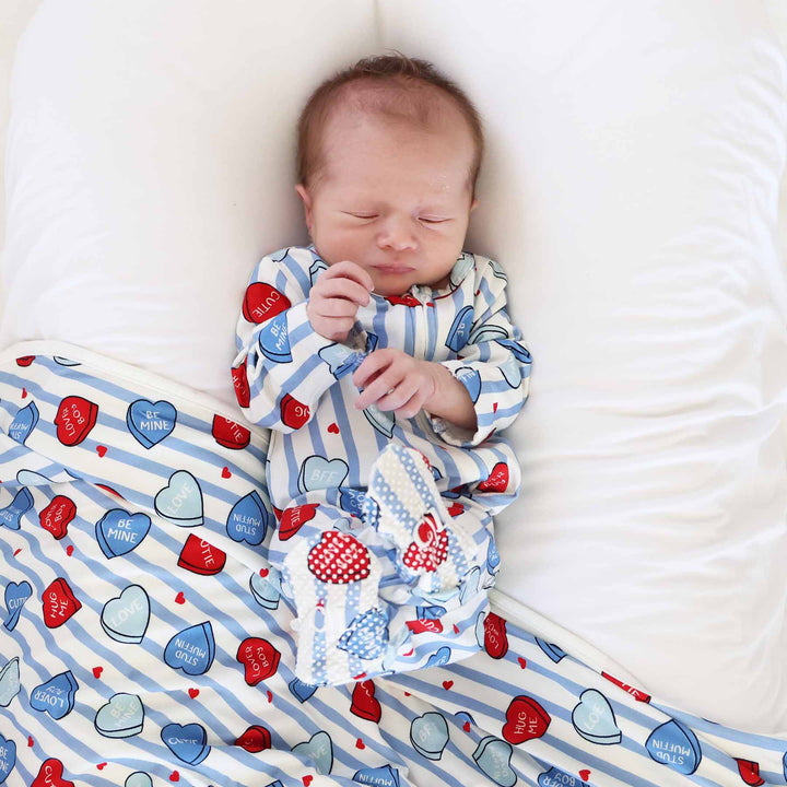 baby laying on a bed wearing a blue stripe heart candy footie for valentine's day with a matching bamboo blanket underneath him