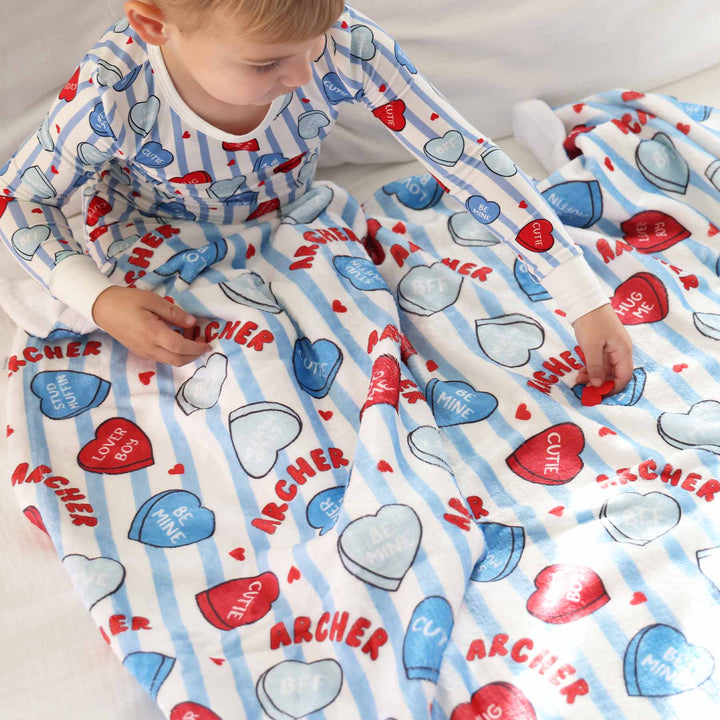 boy wearing a blue stripe and candy heart two piece pajama set with a matching personalized blanket across his lap