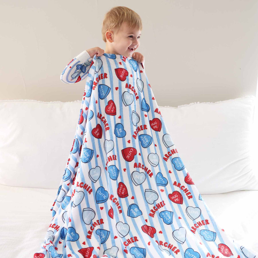 boy standing on bed holding a blue stripe valentine's day candy heart personalized blanket 