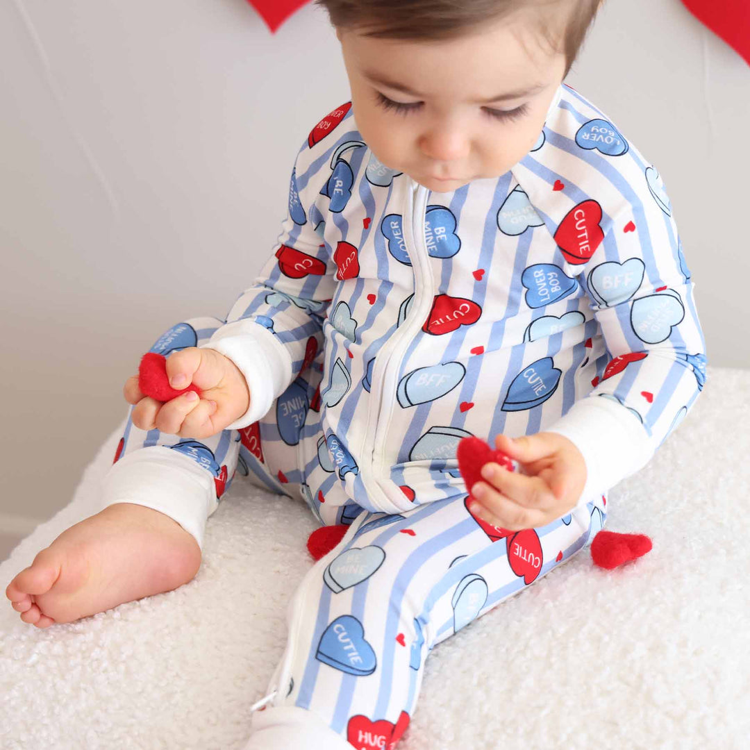boy wearing a valentine's day candy heart pajama romper holding heart confetti