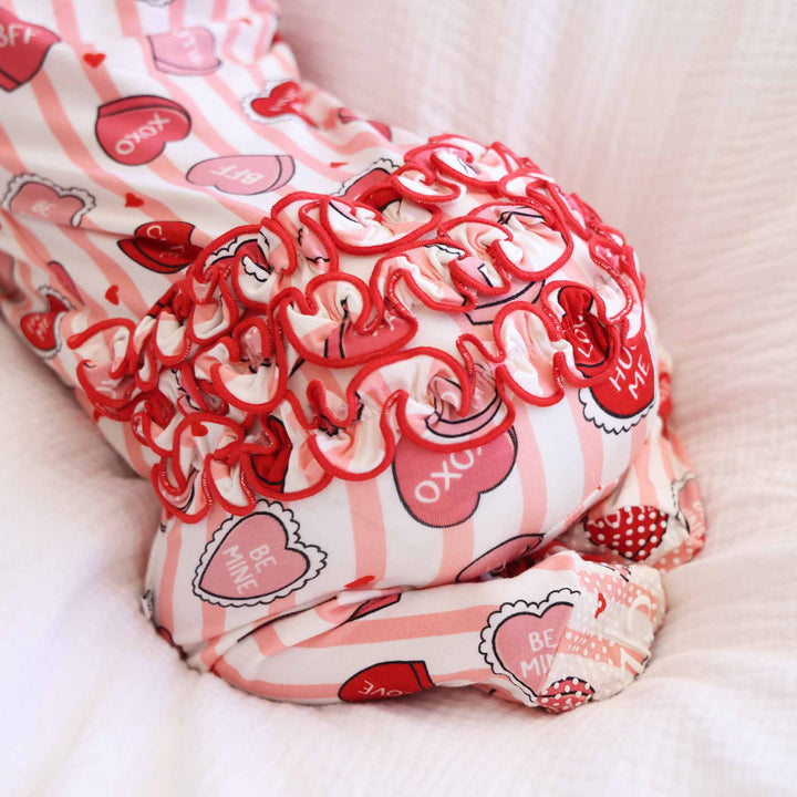closeup of ruffle bottom zipper footie with pink stripes and candy conversation hearts for valentine's day 