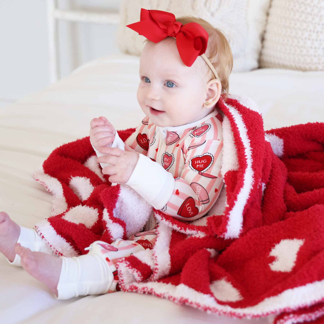 baby girl sitting on a bed in a pink and white stripe pajama romper with pink and red conversation heart candy for valentine's day 