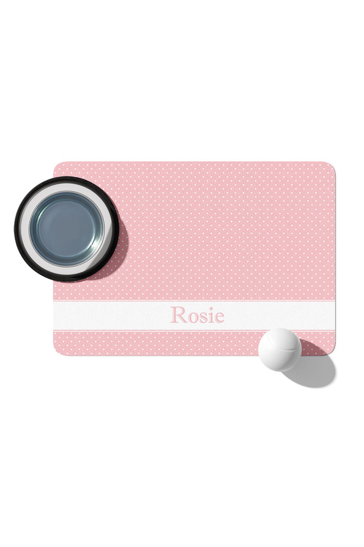 Pink polka dot pet placemat with white name banner reading Rosie in pink lettering, styled with a pet bowl and ball