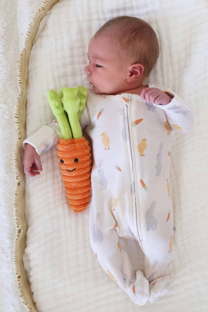 baby boy laying on swaddle blanket in sweet peep bamboo waffle footie next to a carrot stuffed animal