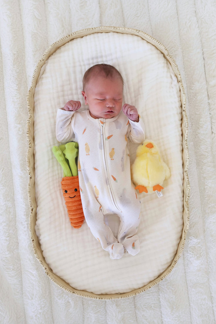 baby wearing sweet peep neutral bamboo waffle zipper footie laying next to a stuffed carrot and chick