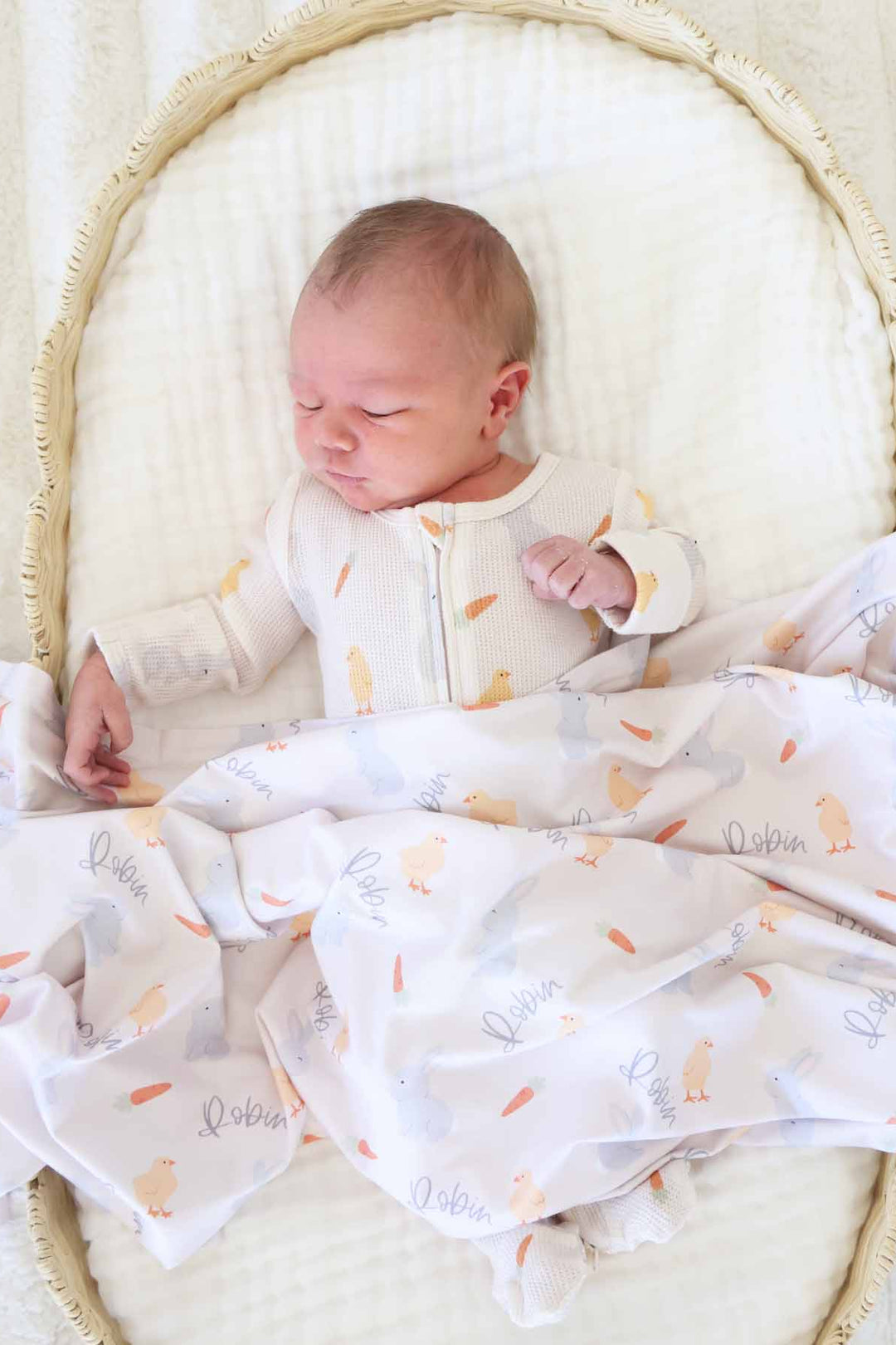 baby laying in basket in sweet peep bamboo waffle zipper footie pajama with a personalized swaddle blanket on top of him