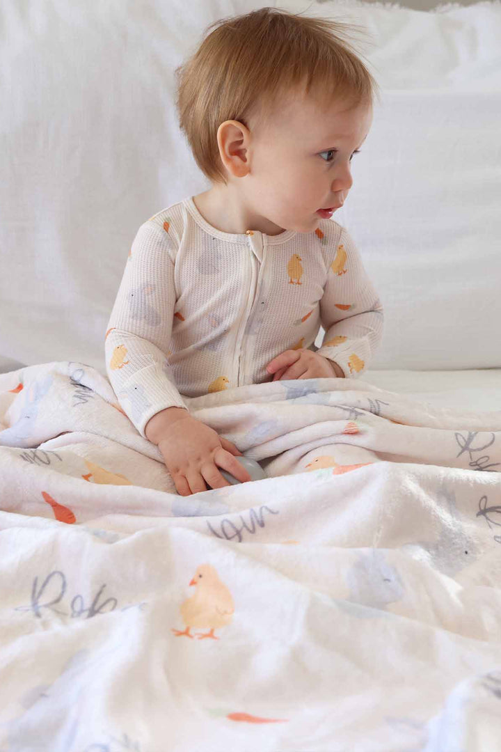 baby boy wearing the sweet peep bamboo waffle convertible zip romper with a matching personalized blanket across his lap
