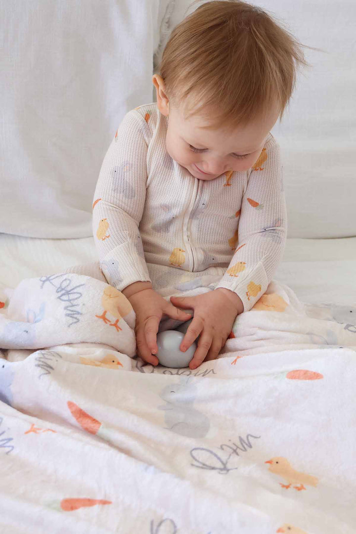 baby boy wearing the sweet peep convertible zip romper holding an easter egg with a matching personalized blanket sitting across their lap